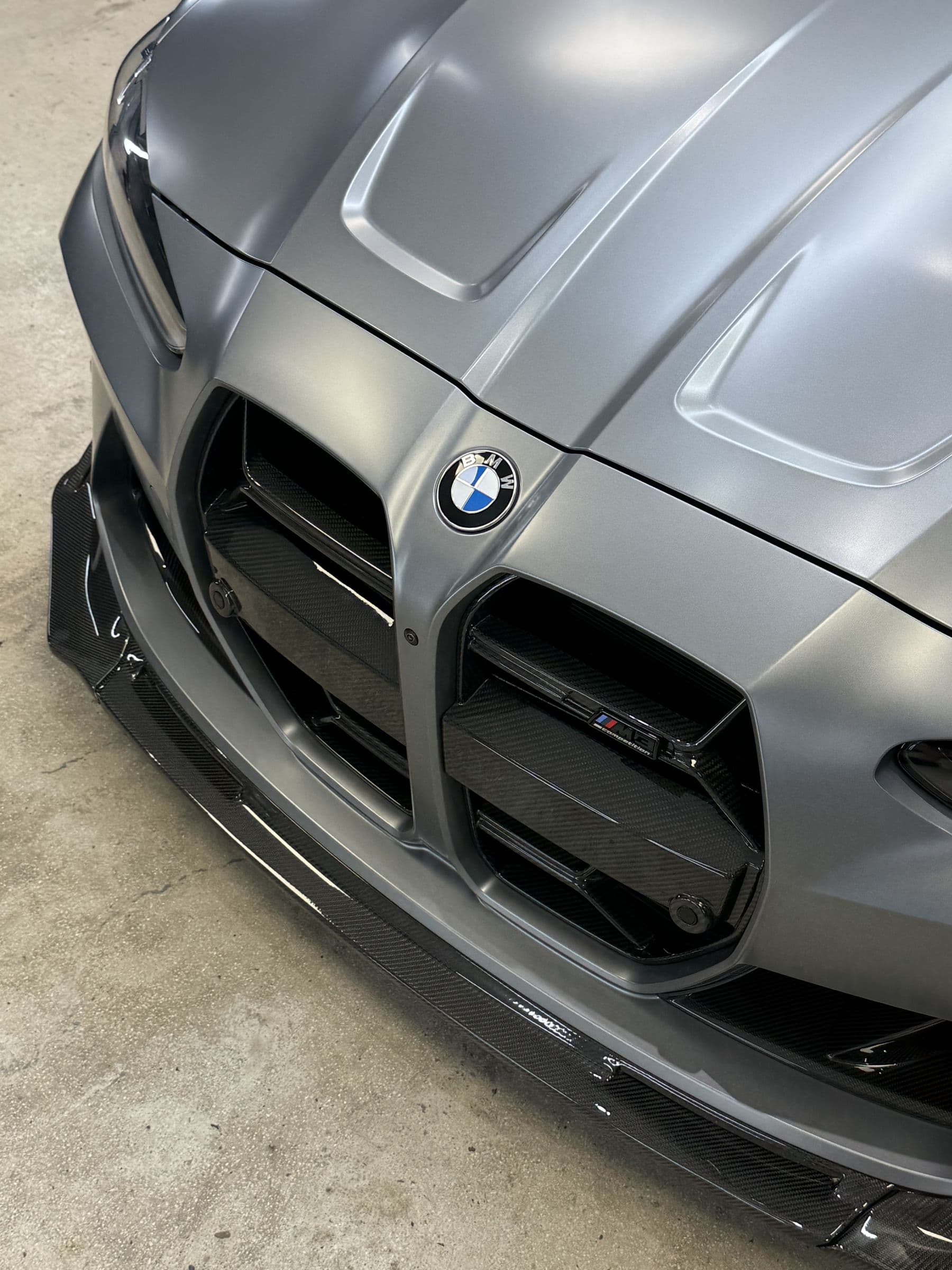 BMW M4 Competition gris mate — detalle del bonete, parrilla y splitter de carbono